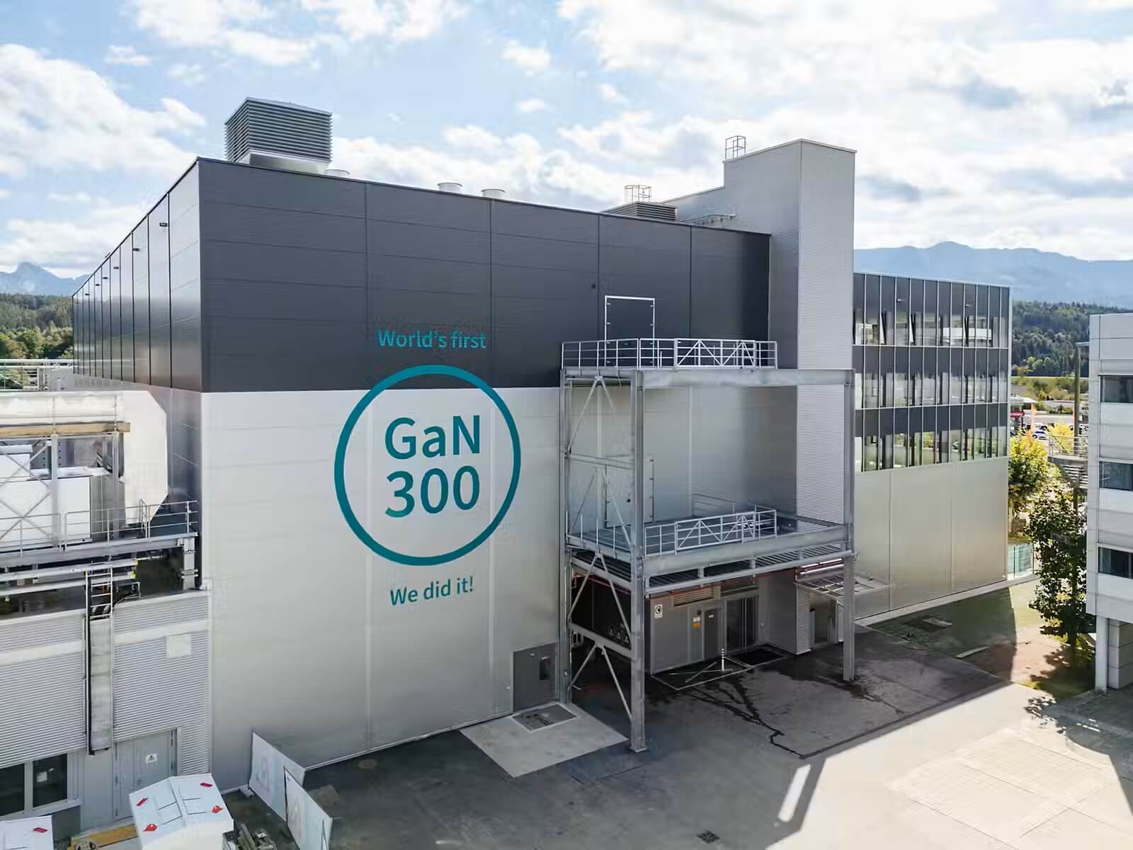 Modern industrial building with a large GaN300 logo on the white wall and the words 'World's first' and 'We did it!' visible; a grey high-tech facility against a blue sky.